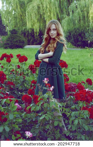 Mysterious caucasian woman with green eyes and green dress looking at the camera surrounded by scarlet roses