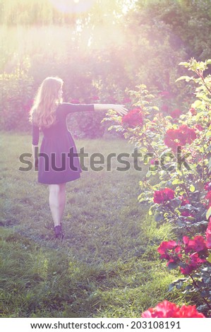 Young woman with auburn hair walking near rose bushes in the sunset light