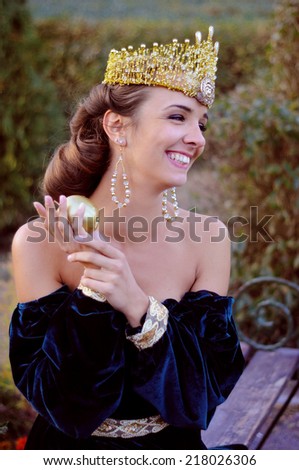 Smiling young woman dressed like queen with a crown  holding a golden apple