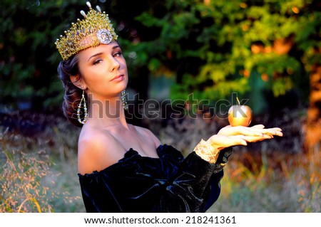 Elegant young woman dressed like queen with a crown holding an apple