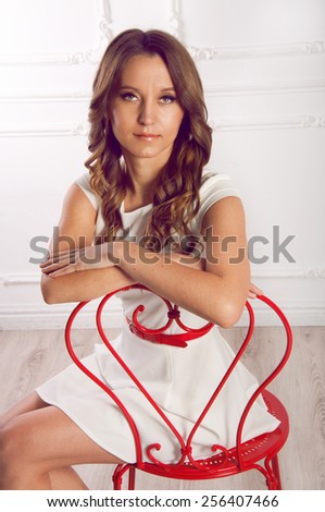 Cute young woman with chestnut hair in white dress and red belt and red shoes