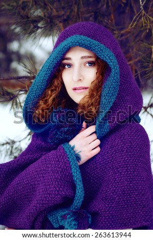 Mysterious young woman in purple knitted cape with a hood in winter forest