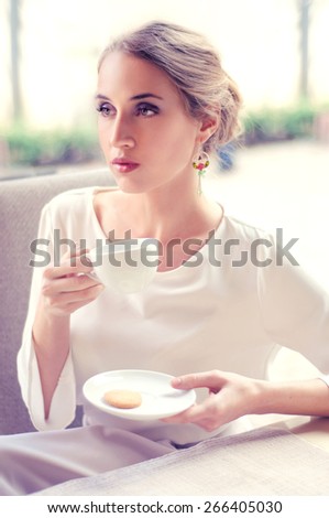 Beautiful elegant blonde sitting in a cafe drinking tea waiting for someone, shallow depth of field.