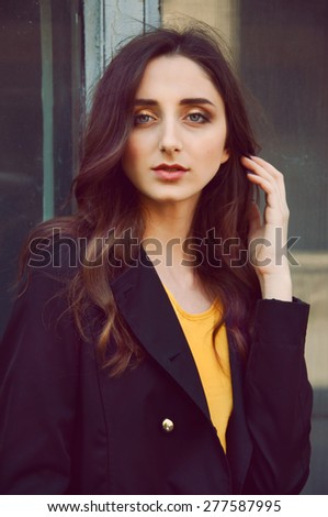 Young woman portrait with long brown hair dressed in black trenchcoat and yellow blouse