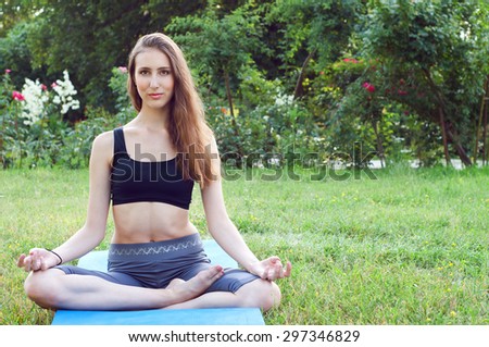 Sportswoman with long hair meditating on a yoga mat outdoor in summer afternoon