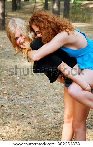 Two girlfriends having fun and smiling piggyback in the park