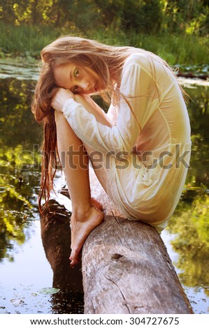 Redhead woman sitting on a tree bark near river in wet blouse