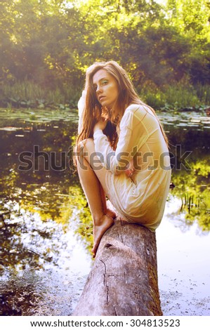 Redhead woman sitting on a tree bark near river in wet blouse