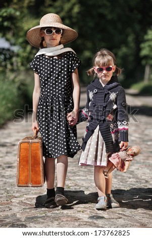 Two retro styled child girls walk together at a road in the countryside/Travelling Child Girls
