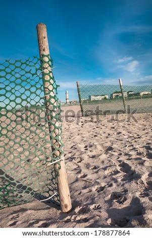 Green net fences at a beach with small gateway view to a lighthouse/Fence Gap View