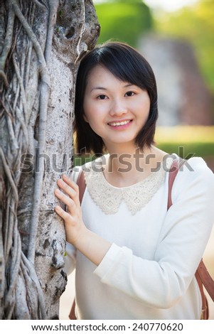 Young smiling asian woman lean to and touch a tree/Beautiful Smiling Natural-Looking Asian Woman