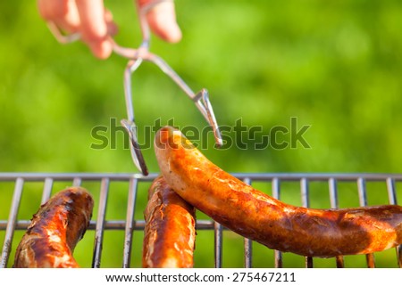 Hand hold tongs for food with at barbecue grill/Grilled Sausages at a Garden Barbecue