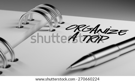 Closeup of a personal agenda setting an important date writing with pen. The words Organize a Trip written on a white notebook to remind you an important appointment.