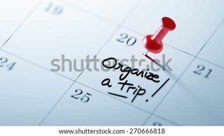 Concept image of a Calendar with a red push pin. Closeup shot of a thumbtack attached. The words Organize a Trip written on a white notebook to remind you an important appointment.
