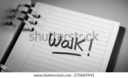 Closeup of a personal agenda setting an important date representing a time schedule. The words Walk written on a white notebook to remind you an important appointment.