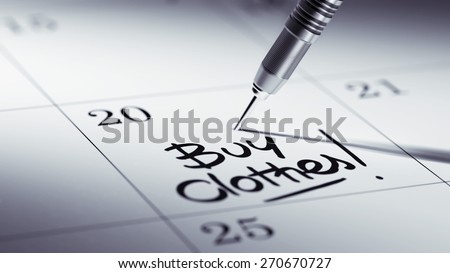 Concept image of a Calendar with a golden dart stick. The words Buy Clothes written on a white notebook to remind you an important appointment.