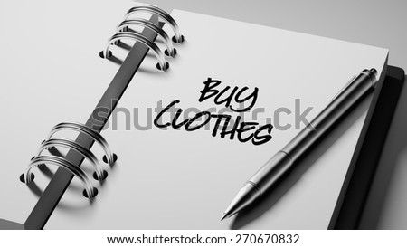 Closeup of a personal agenda setting an important date writing with pen. The words Buy Clothes written on a white notebook to remind you an important appointment.
