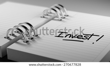 Closeup of a personal agenda setting an important date representing a time schedule. The words Invest written on a white notebook to remind you an important appointment.