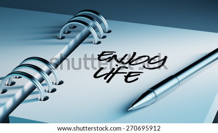 Closeup of a personal agenda setting an important date writing with pen. The words Enjoy Life written on a white notebook to remind you an important appointment.
