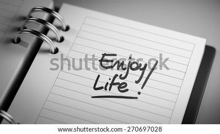 Closeup of a personal agenda setting an important date representing a time schedule. The words Enjoy Life written on a white notebook to remind you an important appointment.