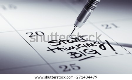 Concept image of a Calendar with a golden dart stick. The words Start thinking BIG written on a white notebook to remind you an important appointment.