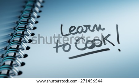 Closeup of a personal calendar setting an important date representing a time schedule. The words Learn to Cook written on a white notebook to remind you an important appointment.