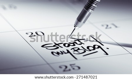 Concept image of a Calendar with a golden dart stick. The words Start my Blog written on a white notebook to remind you an important appointment.