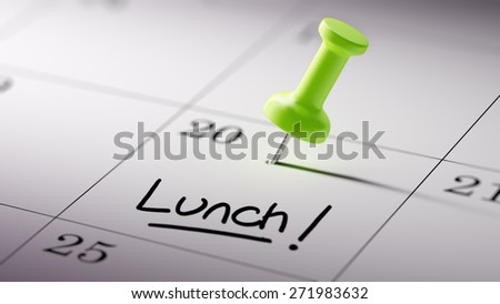 Concept image of a Calendar with a green push pin. Closeup shot of a thumbtack attached. The words Lunch written on a white notebook to remind you an important appointment.