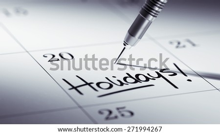 Concept image of a Calendar with a golden dart stick. The words Holidays written on a white notebook to remind you an important appointment.