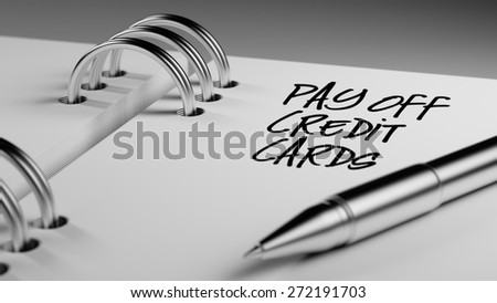 Closeup of a personal agenda setting an important date writing with pen. The words Pay off Credit cards written on a white notebook to remind you an important appointment.