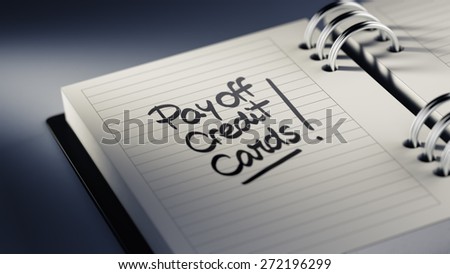 Closeup of a personal agenda setting an important date representing a time schedule. The words Pay off Credit cards written on a white notebook to remind you an important appointment.