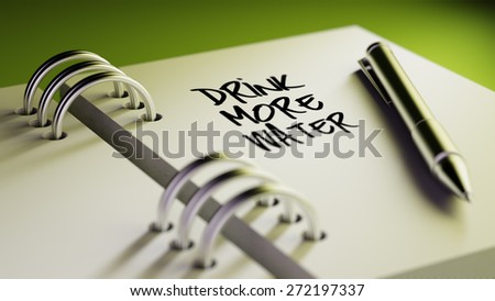 Closeup of a personal agenda setting an important date writing with pen. The words Drink more water written on a white notebook to remind you an important appointment.