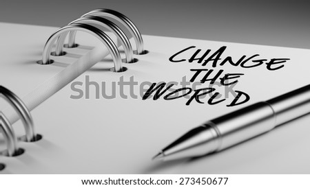 Closeup of a personal agenda setting an important date writing with pen. The words Change the world written on a white notebook to remind you an important appointment.