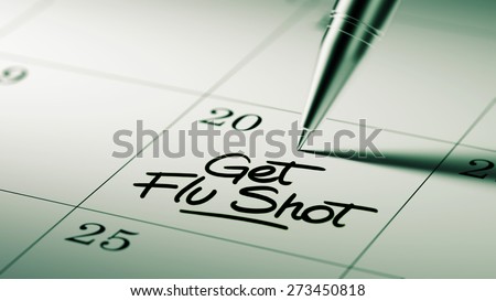 Closeup of a personal agenda setting an important date written with pen. The words Get Flu Shot written on a white notebook to remind you an important appointment.