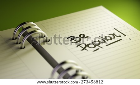 Closeup of a personal agenda setting an important date representing a time schedule. The words Be Popular written on a white notebook to remind you an important appointment.