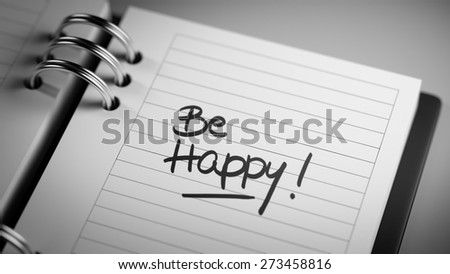 Closeup of a personal agenda setting an important date representing a time schedule. The words Be happy written on a white notebook to remind you an important appointment.
