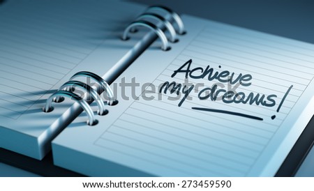 Closeup of a personal agenda setting an important date representing a time schedule. The words Achieve my dreams written on a white notebook to remind you an important appointment.