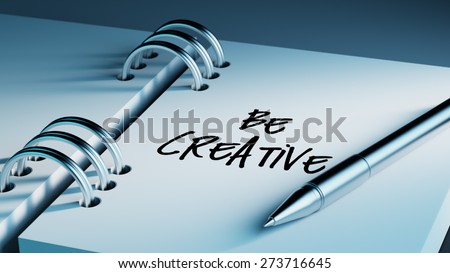 Closeup of a personal agenda setting an important date writing with pen. The words Be Creative written on a white notebook to remind you an important appointment.