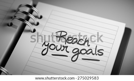 Closeup of a personal agenda setting an important date representing a time schedule. The words Reach your goals written on a white notebook to remind you an important appointment.