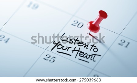 Concept image of a Calendar with a red push pin. Closeup shot of a thumbtack attached. The words Listen to your heart written on a white notebook to remind you an important appointment.
