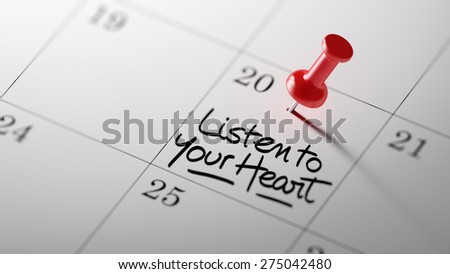 Concept image of a Calendar with a red push pin. Closeup shot of a thumbtack attached. The words Listen to your heart written on a white notebook to remind you an important appointment.