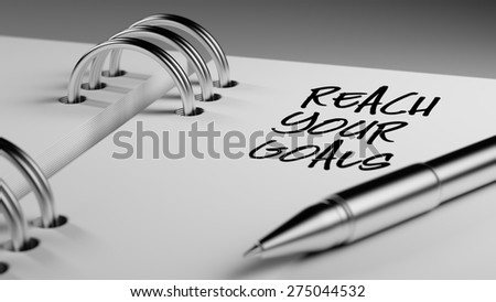 Closeup of a personal agenda setting an important date writing with pen. The words Reach your goals written on a white notebook to remind you an important appointment.