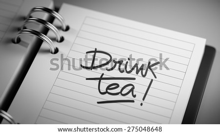 Closeup of a personal agenda setting an important date representing a time schedule. The words Drink Tea written on a white notebook to remind you an important appointment.