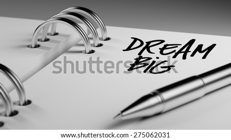 Closeup of a personal agenda setting an important date writing with pen. The words Dream big written on a white notebook to remind you an important appointment.