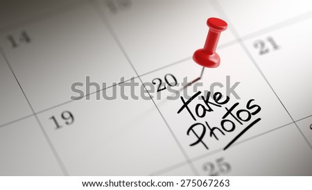 Concept image of a Calendar with a red push pin. Closeup shot of a thumbtack attached. The words Take photos written on a white notebook to remind you an important appointment.