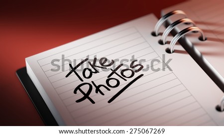 Closeup of a personal agenda setting an important date representing a time schedule. The words Take photos written on a white notebook to remind you an important appointment.