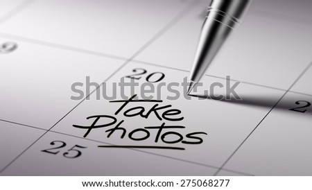 Closeup of a personal agenda setting an important date written with pen. The words Take photos written on a white notebook to remind you an important appointment.