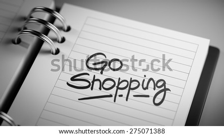 Closeup of a personal agenda setting an important date representing a time schedule. The words Go shopping written on a white notebook to remind you an important appointment.