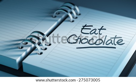 Closeup of a personal agenda setting an important date representing a time schedule. The words Eat Chocolate written on a white notebook to remind you an important appointment.