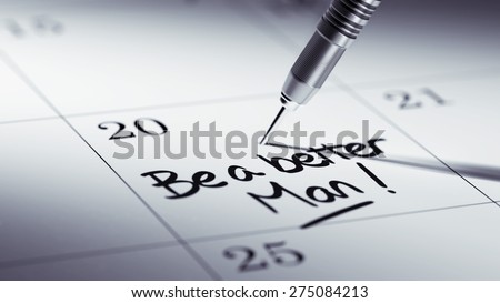 Concept image of a Calendar with a golden dart stick. The words Be a better man written on a white notebook to remind you an important appointment.